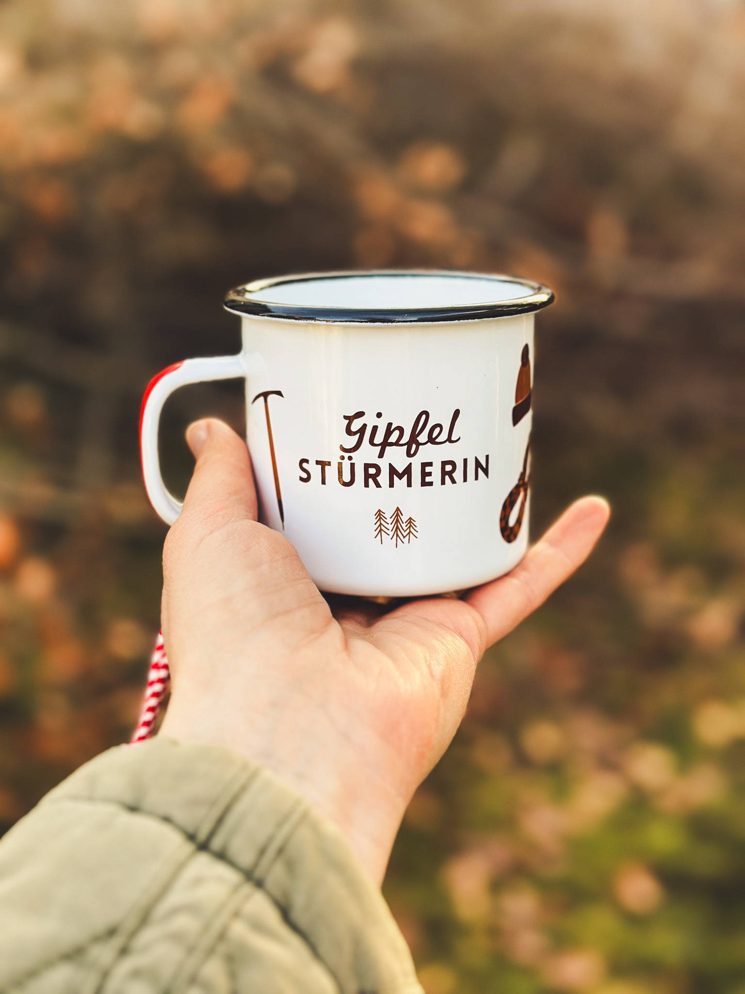 weiße Emaille Tasse mit schwarzen Rand und der Aufschrift Gipfel Stürmerin in der Hand einer Person